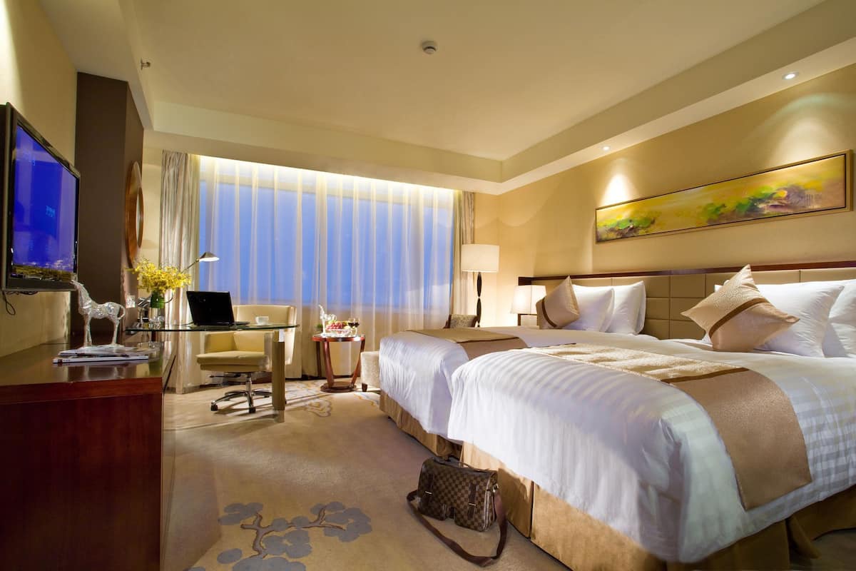 Une chambre d’hôtel avec un lit, un bureau avec un ordinateur portable, une télévision et une fenêtre avec des rideaux.