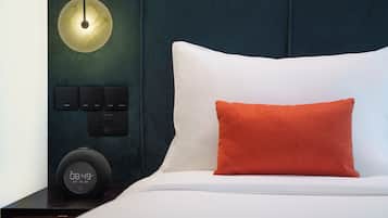 A modern bedroom with a white bed, a red pillow, a bedside table with a clock, and a wall-mounted light fixture.