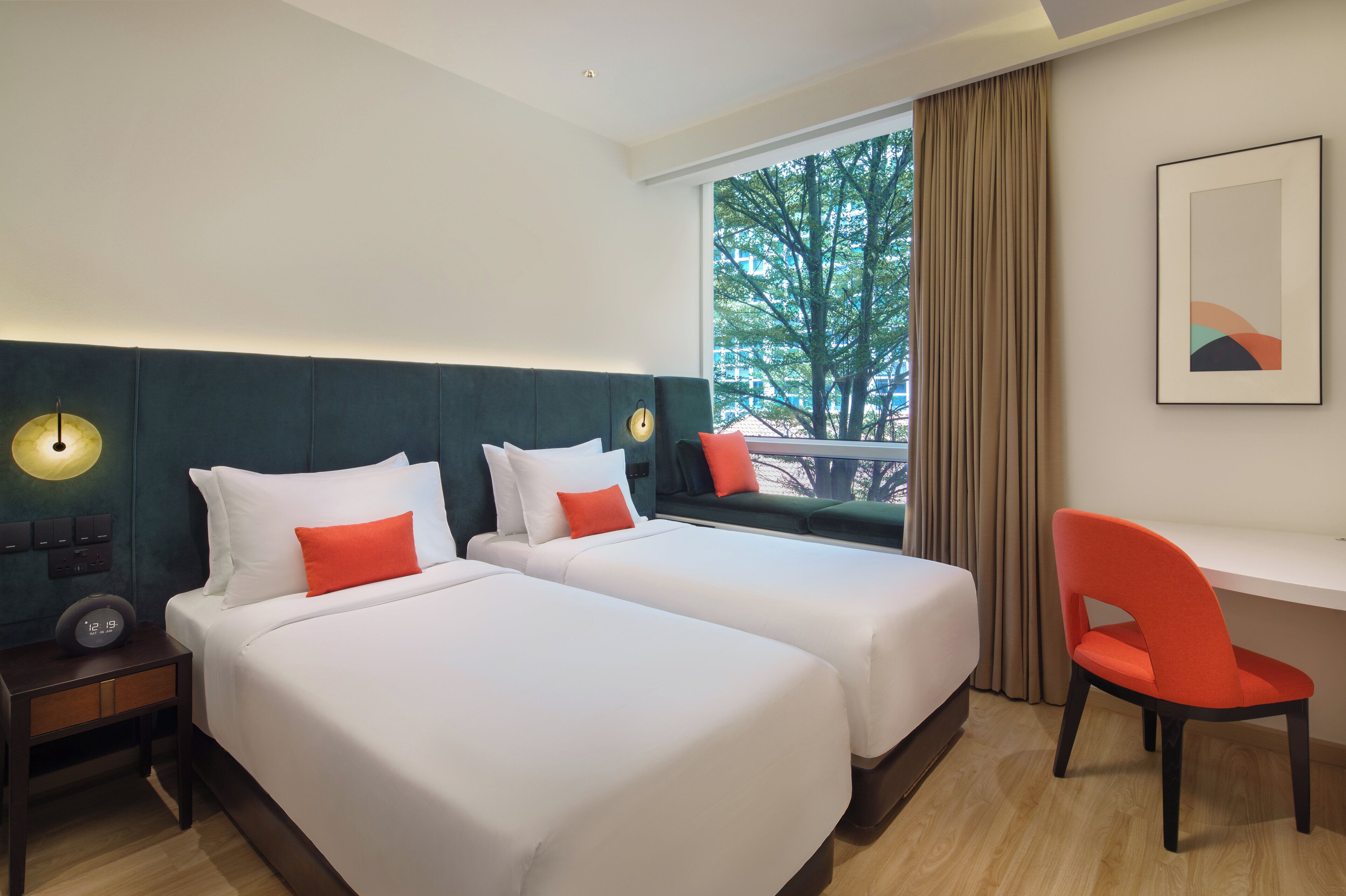 A hotel room with two beds, a desk, a chair, a clock, and a window with a view of trees.