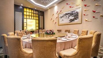 A conference room with a round table, beige upholstered chairs, a floral centerpiece, and a framed artwork on the wall.