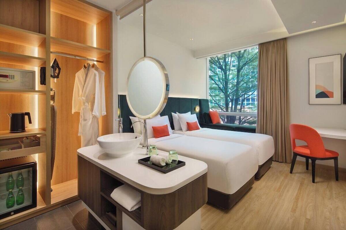 Habitación de hotel con una cama grande, una mesita de noche con espejo, un escritorio pequeño con lavamanos y una silla.