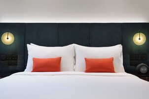 A bed with white and orange pillows, a dark headboard, and wall-mounted light fixtures.
