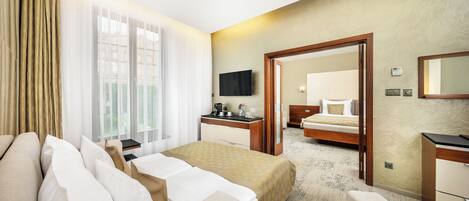 Habitación de hotel con cama, mesita de noche y escritorio con silla. Cuenta con una ventana con cortinas, un televisor de pantalla plana montado en la pared y un espejo sobre el escritorio.