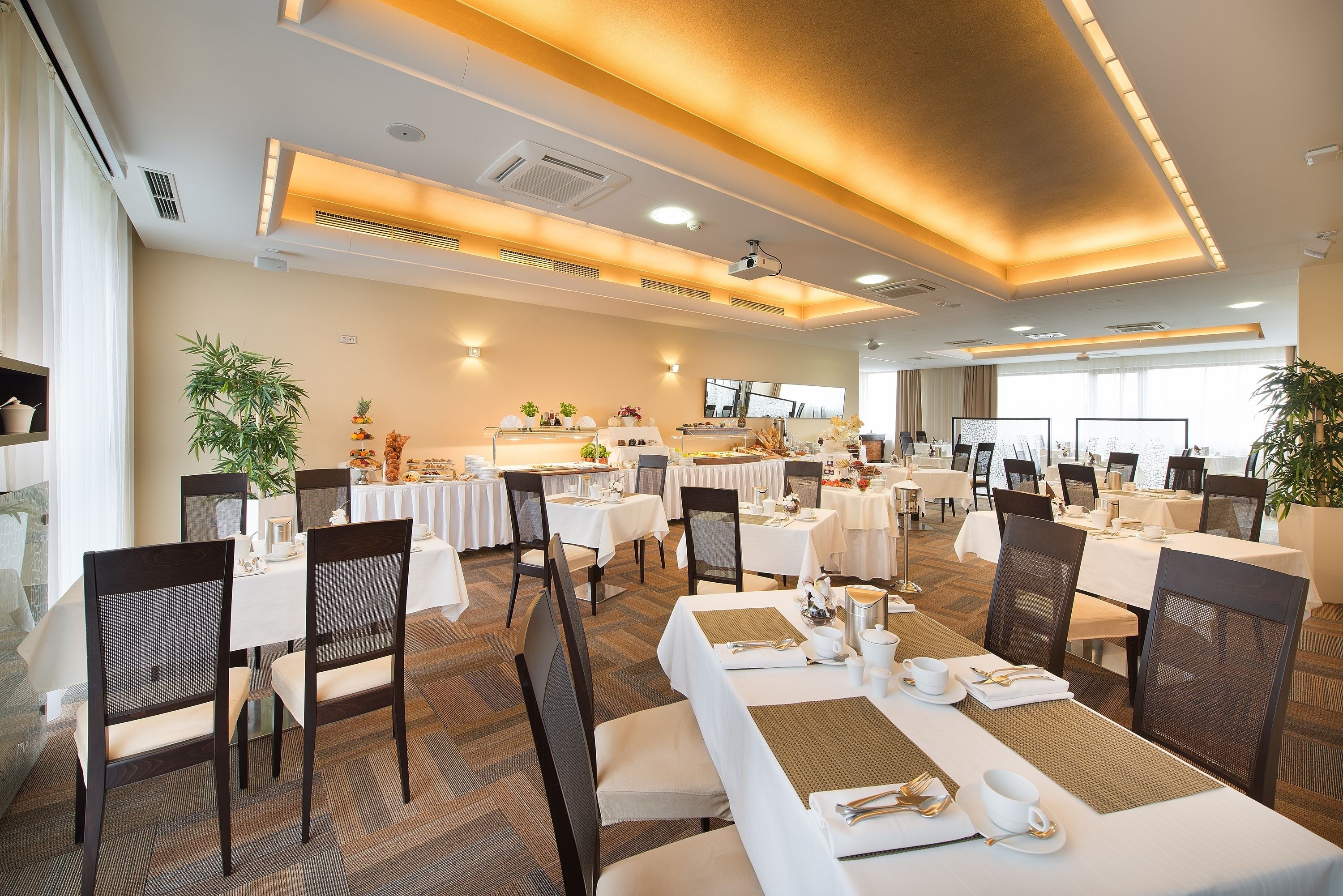 A spacious dining area with multiple tables and chairs, equipped with white tablecloths and gold accents.