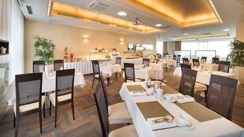 A spacious dining area with multiple tables and chairs, equipped with white tablecloths and gold accents.