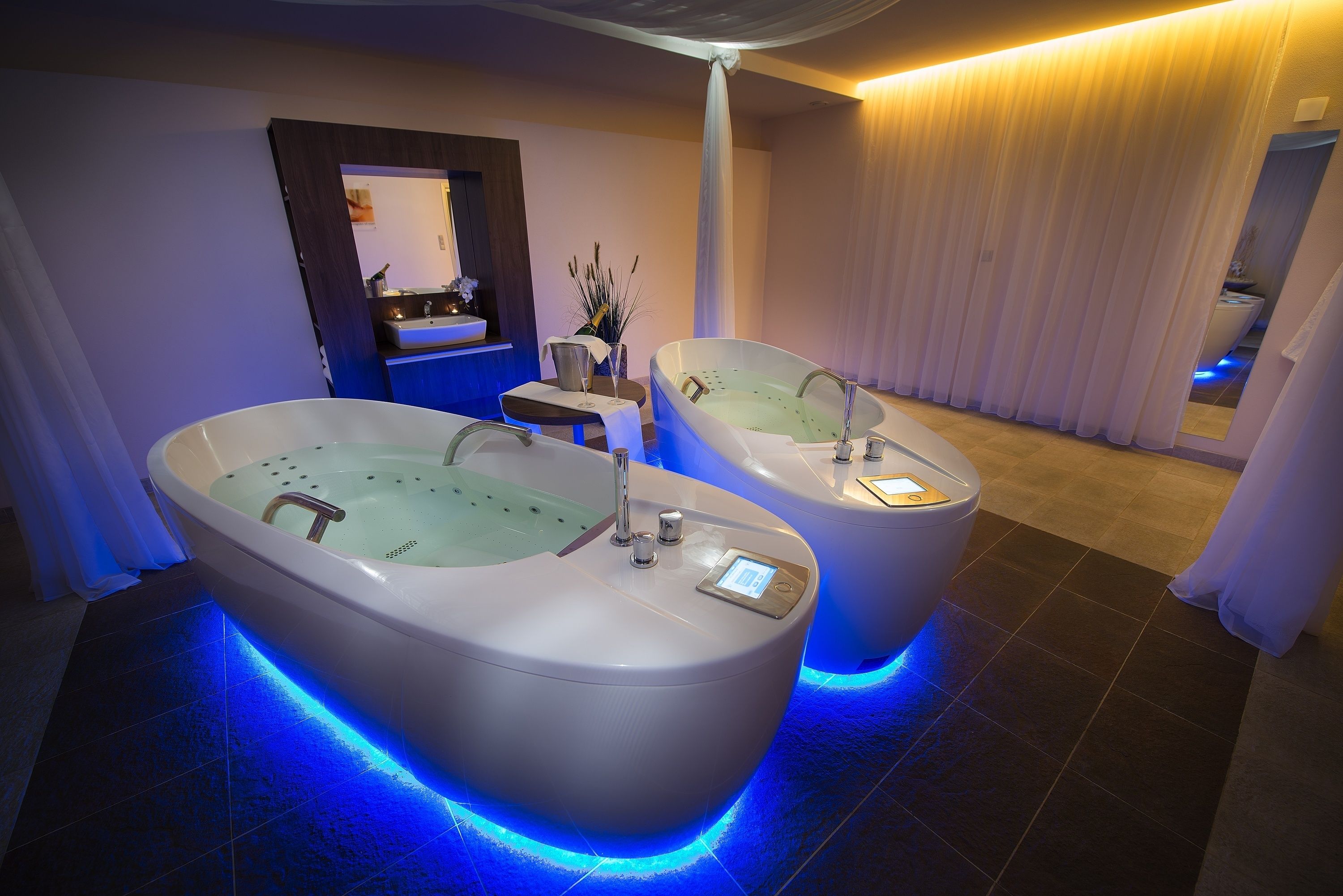 Une salle de spa moderne avec deux grandes baignoires, une coiffeuse avec un miroir et une petite table sur laquelle est posé un vase.