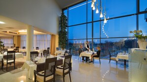 A spacious dining area with tables set for a meal, large windows, and modern lighting fixtures. - Wellness Hotel Diamant (Hluboka nad Vltavou)