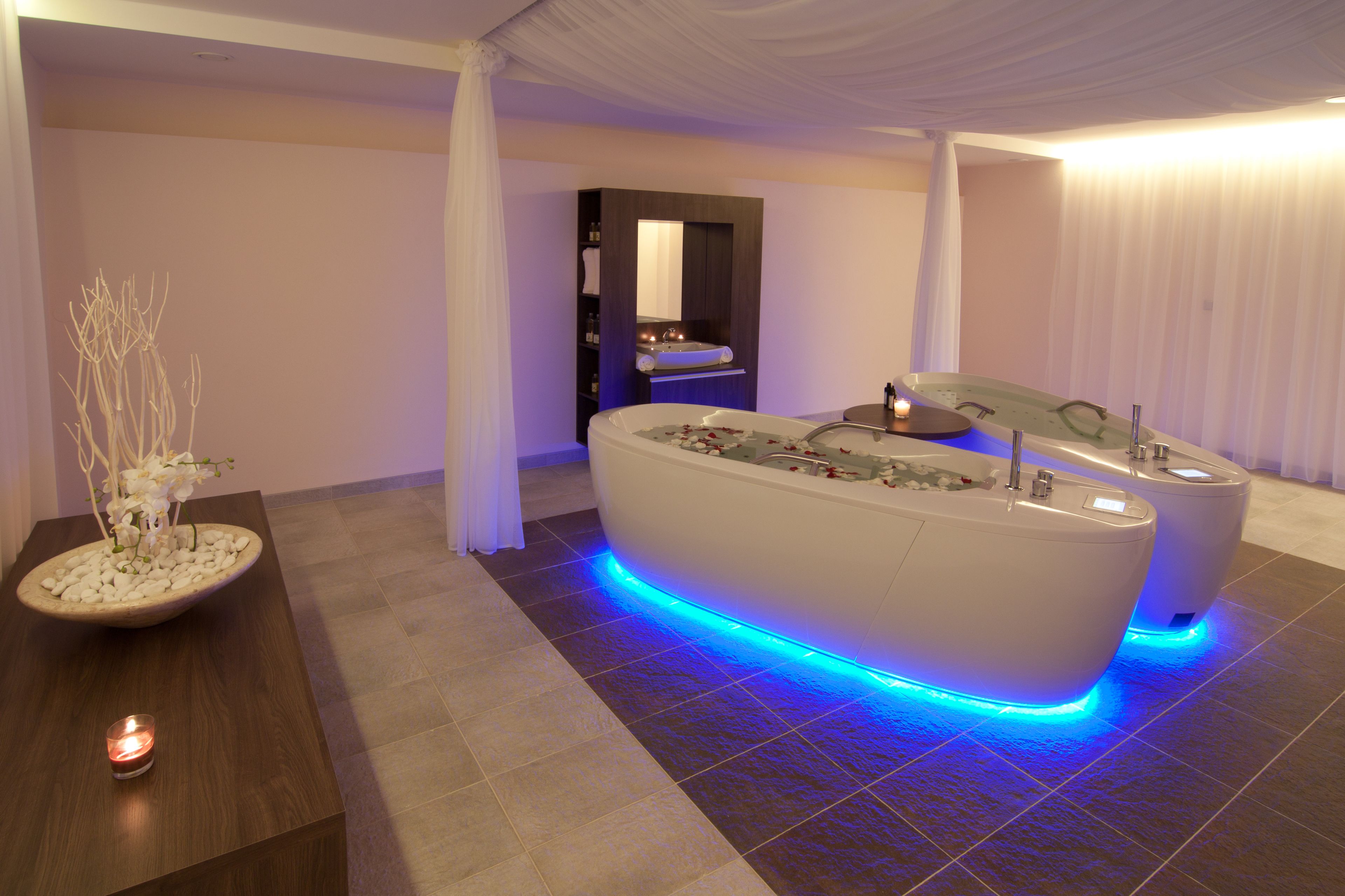 Une salle de bain moderne avec une baignoire sur pieds, un meuble-lavabo avec un miroir et une petite table sur laquelle est posée une bougie.