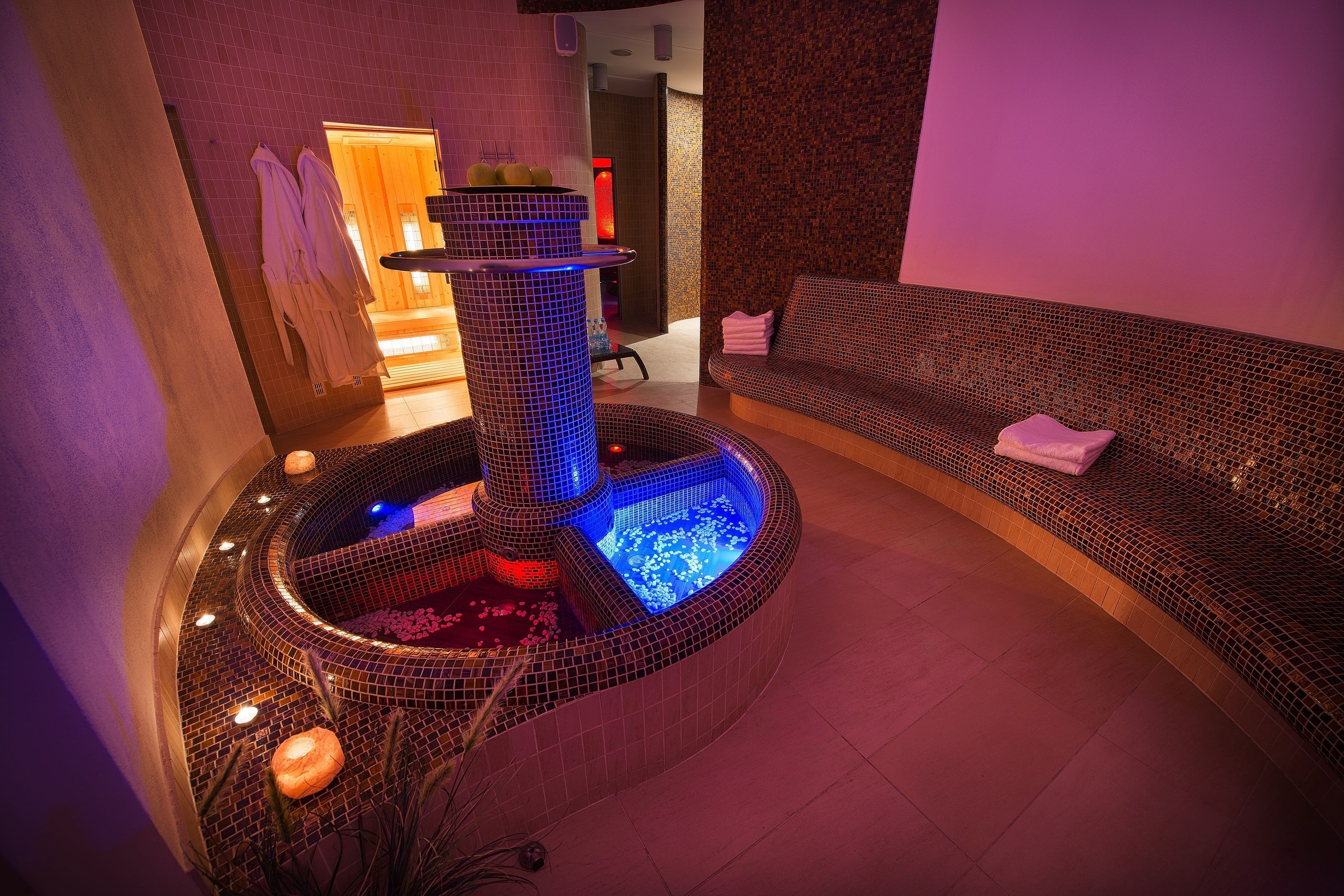 Ein Wellnessbereich mit Whirlpool, Sitzgelegenheiten und einer Wand mit strukturierter Oberfläche.