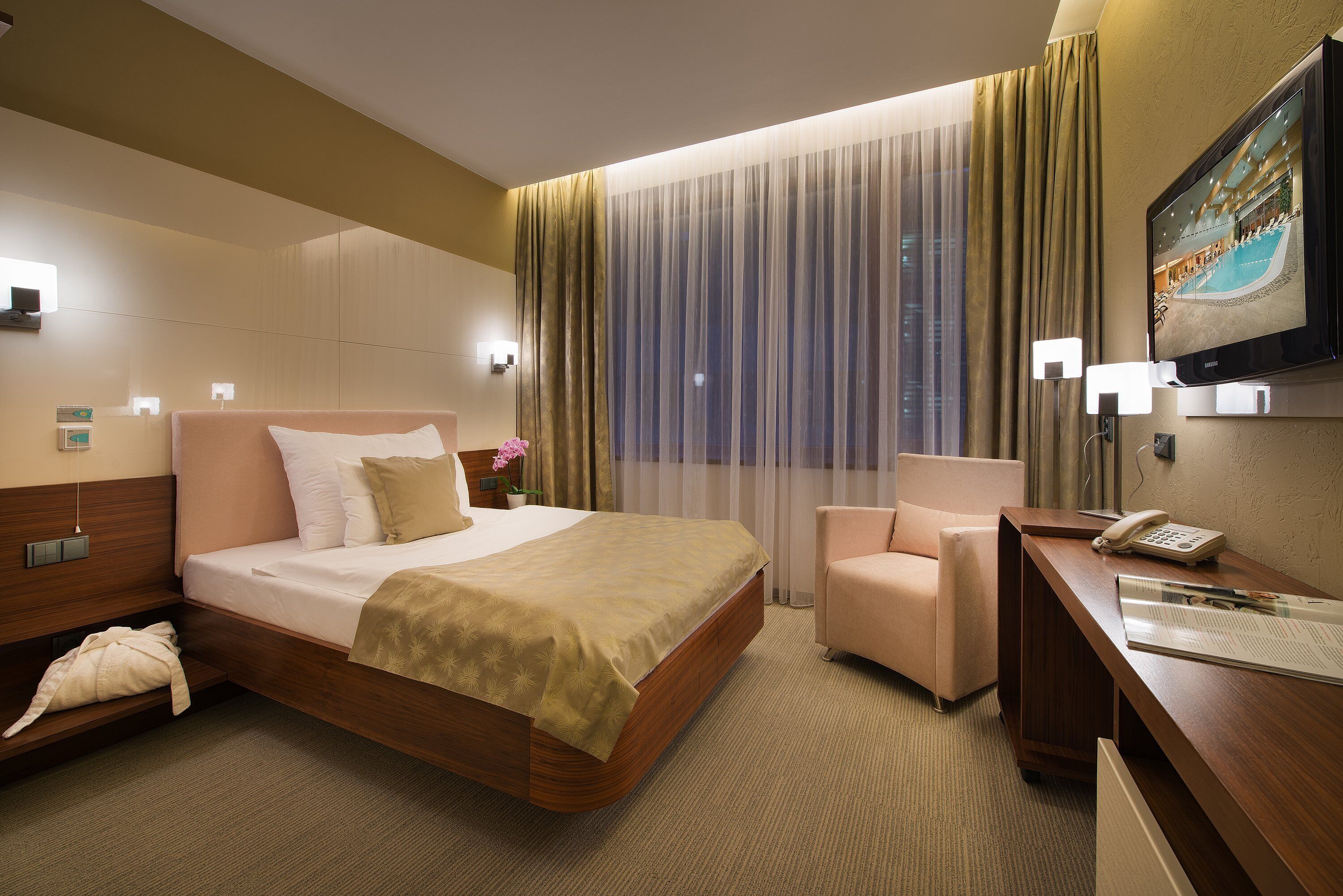 A hotel room with a large bed, a desk, a chair, and a TV on the wall.