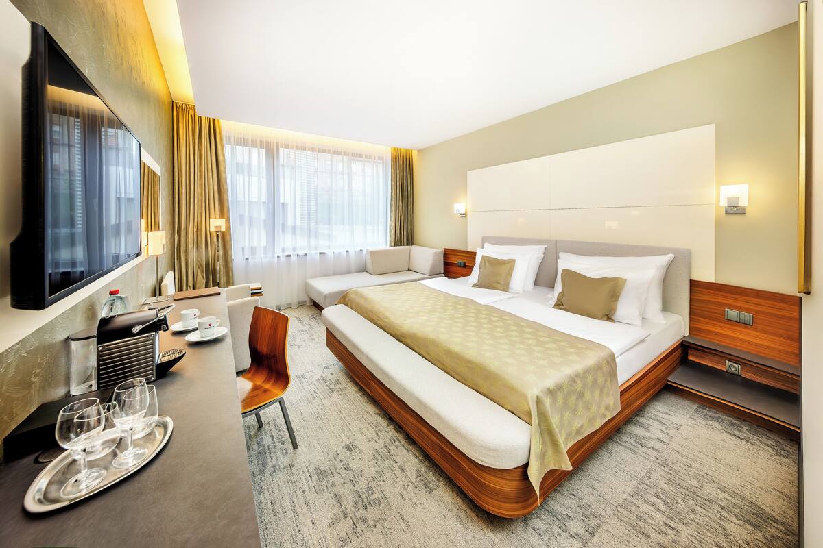 A hotel room with a large bed, a desk with a chair, a TV, and a window with curtains.