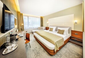 A hotel room with a large bed, a desk with a chair, a TV, and a window with curtains. - Wellness Hotel Diamant (Hluboka nad Vltavou)