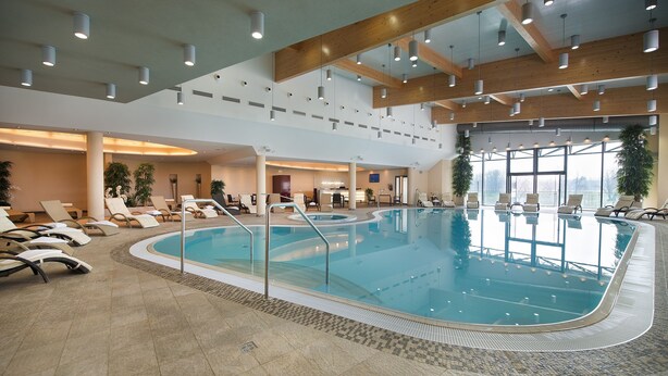 A large indoor swimming pool with lounge chairs and a high ceiling with exposed beams. - Wellness Hotel Diamant (Hluboka nad Vltavou)