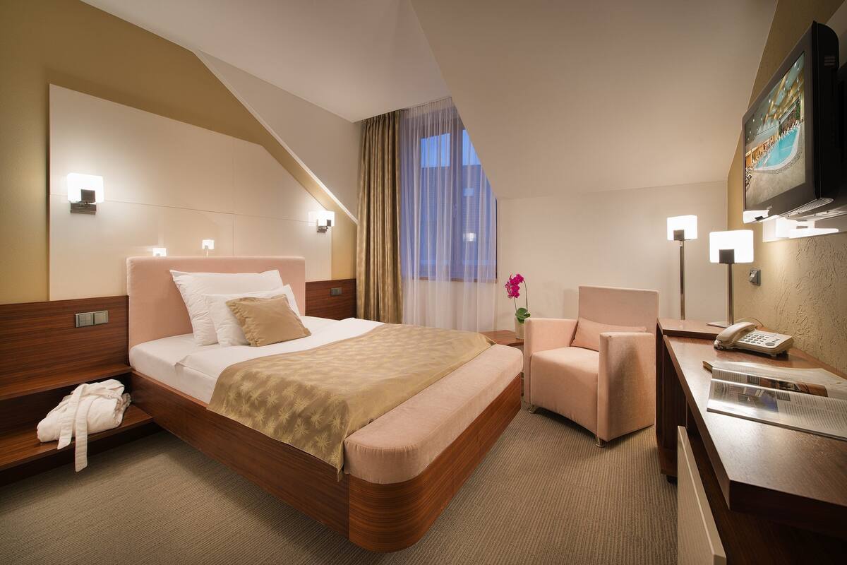 A hotel room with a bed, a desk, a chair, a robe, and a TV.