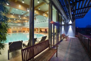 A pool area with lounge chairs and a wooden bench, large windows, and a covered outdoor seating area. - Wellness Hotel Diamant (Hluboka nad Vltavou)