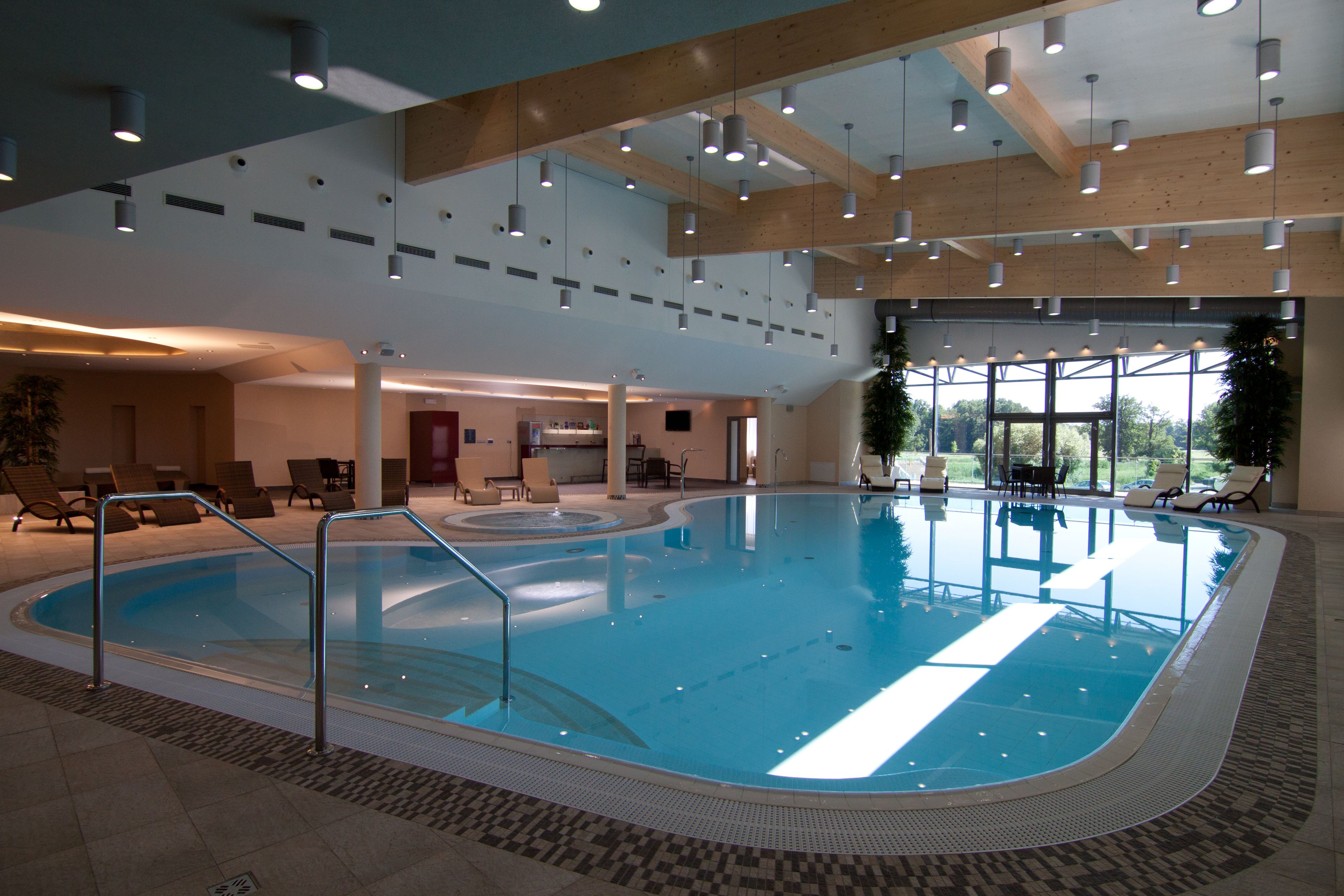An indoor swimming pool with a clear view of the surrounding lounge area, including seating and a view of the outdoors through large windows.
