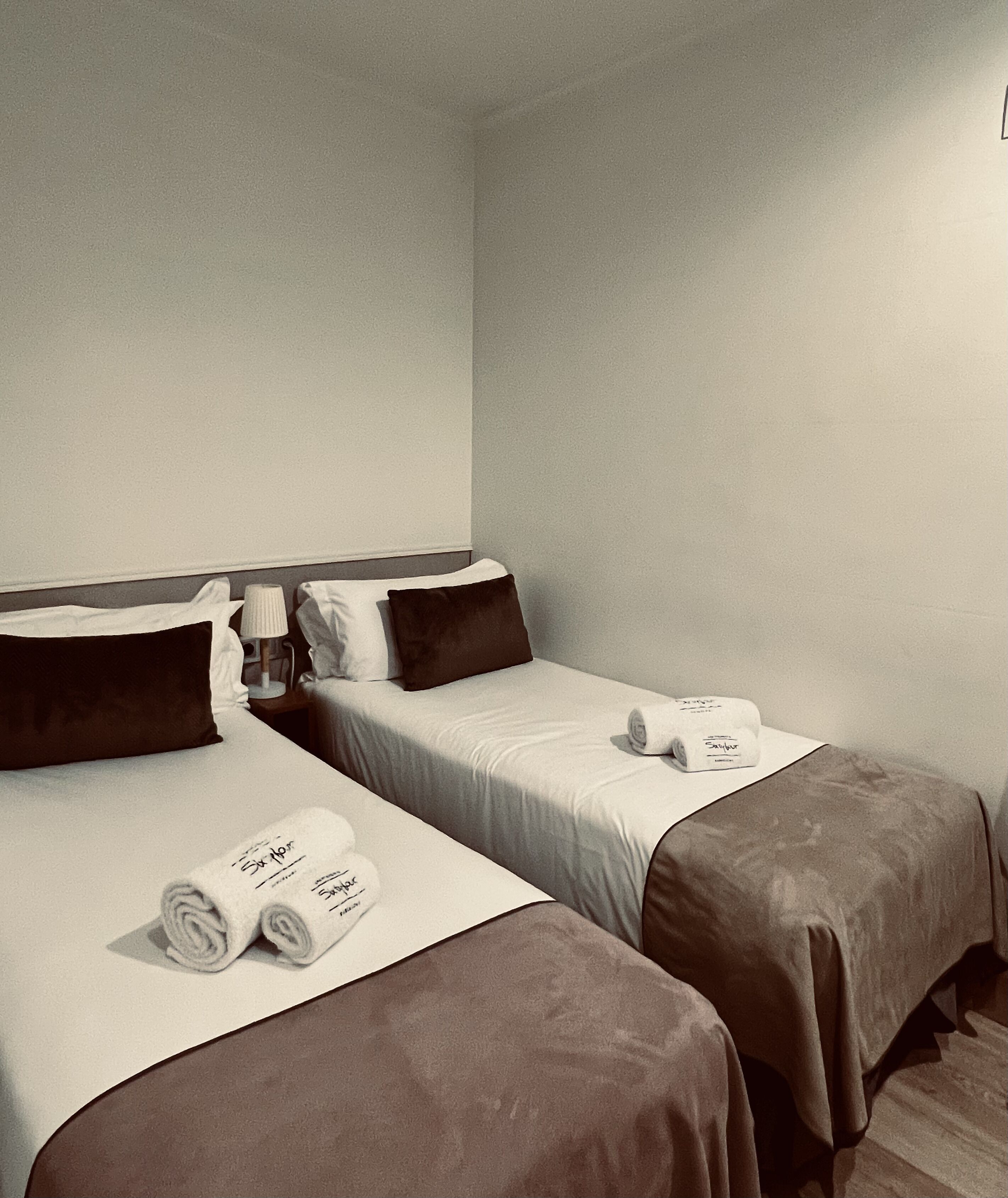 A hotel room with two beds, each with a pillow, a lamp, and rolled towels on the beds.