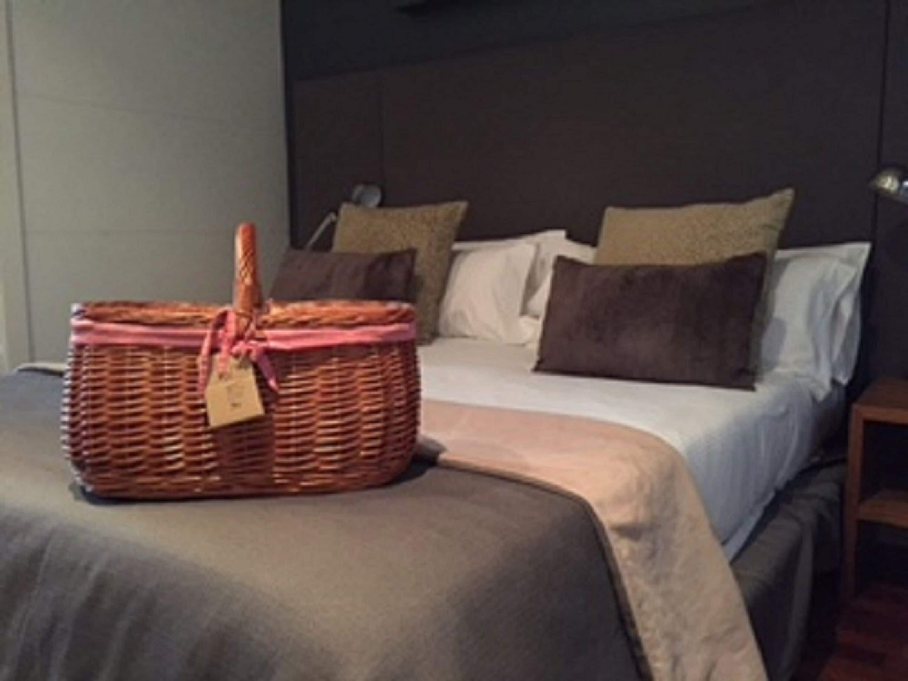 A neatly made bed with a headboard, a bedside table, and a wicker basket with a tag on it.