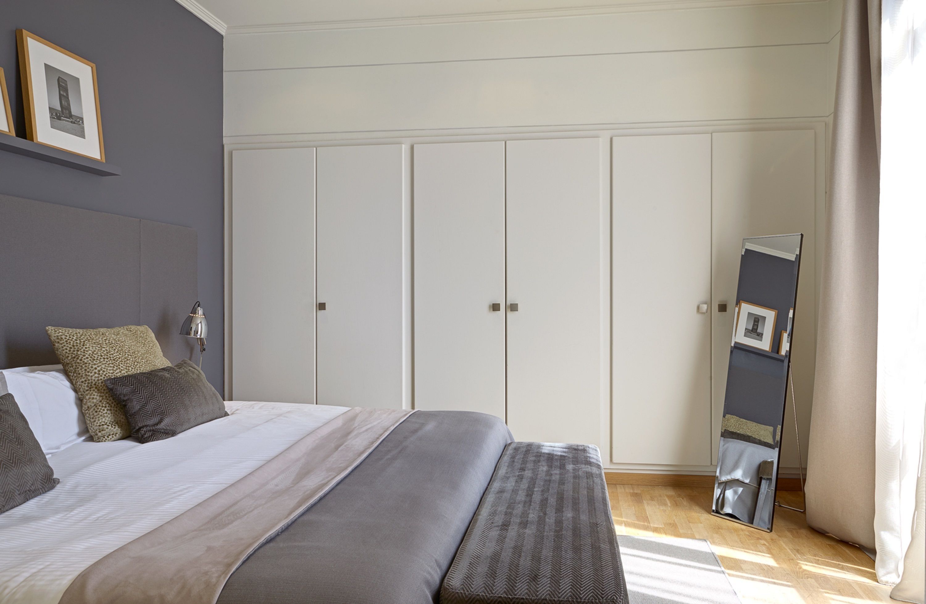 A bedroom with a large bed, a wardrobe, a mirror, and a framed picture on the wall.