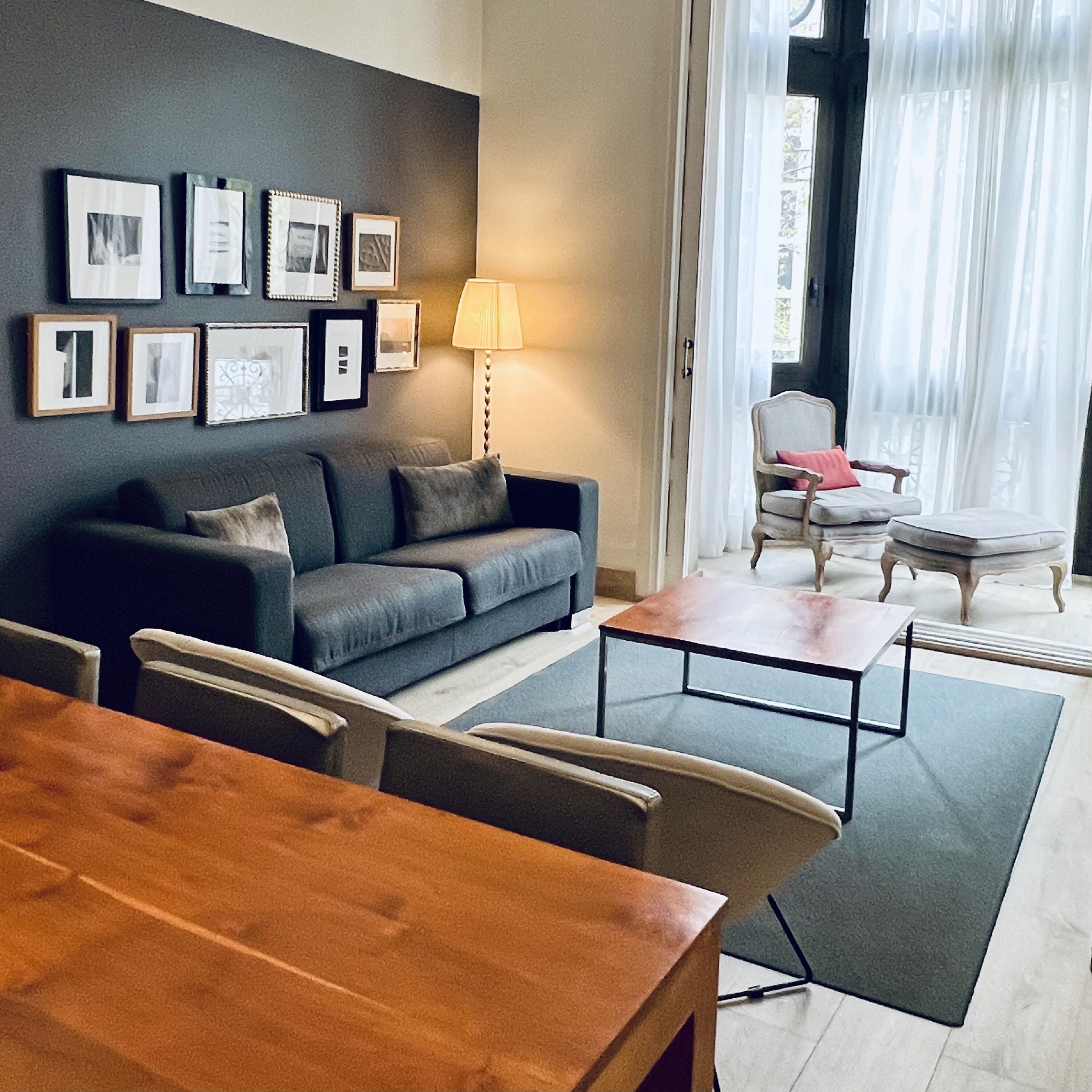 Una sala de estar con un sofá, una mesa de centro y una mesa de comedor. Hay cuadros en la pared y una lámpara.