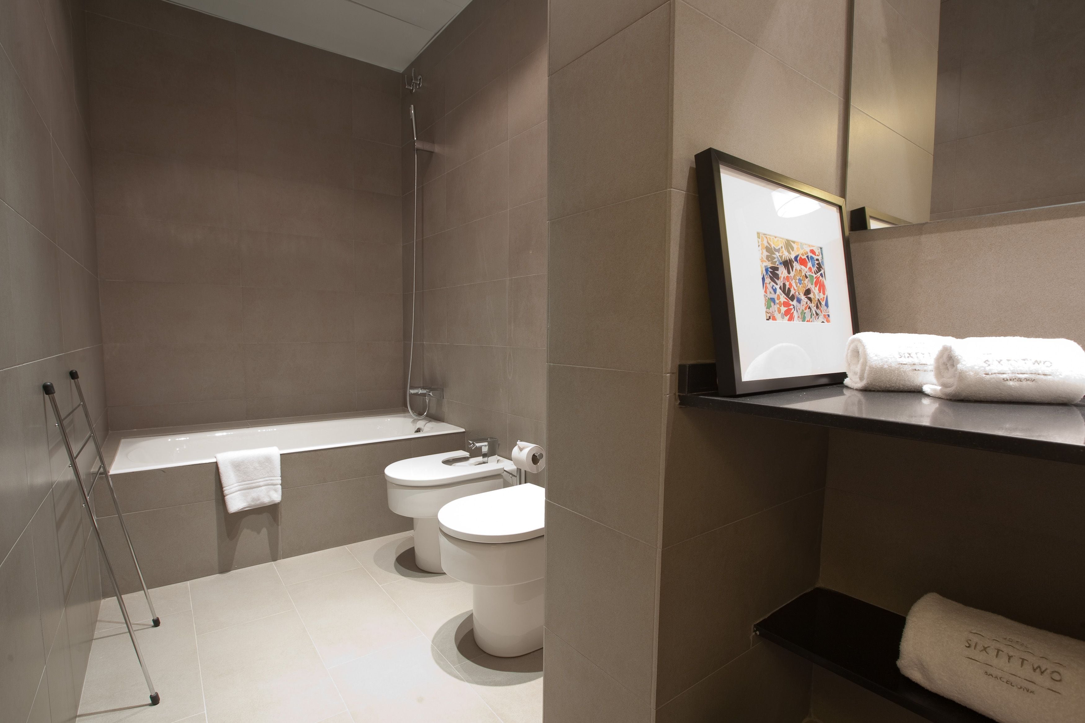 Un baño moderno con bañera, dos inodoros, ducha y un perchero para toallas.