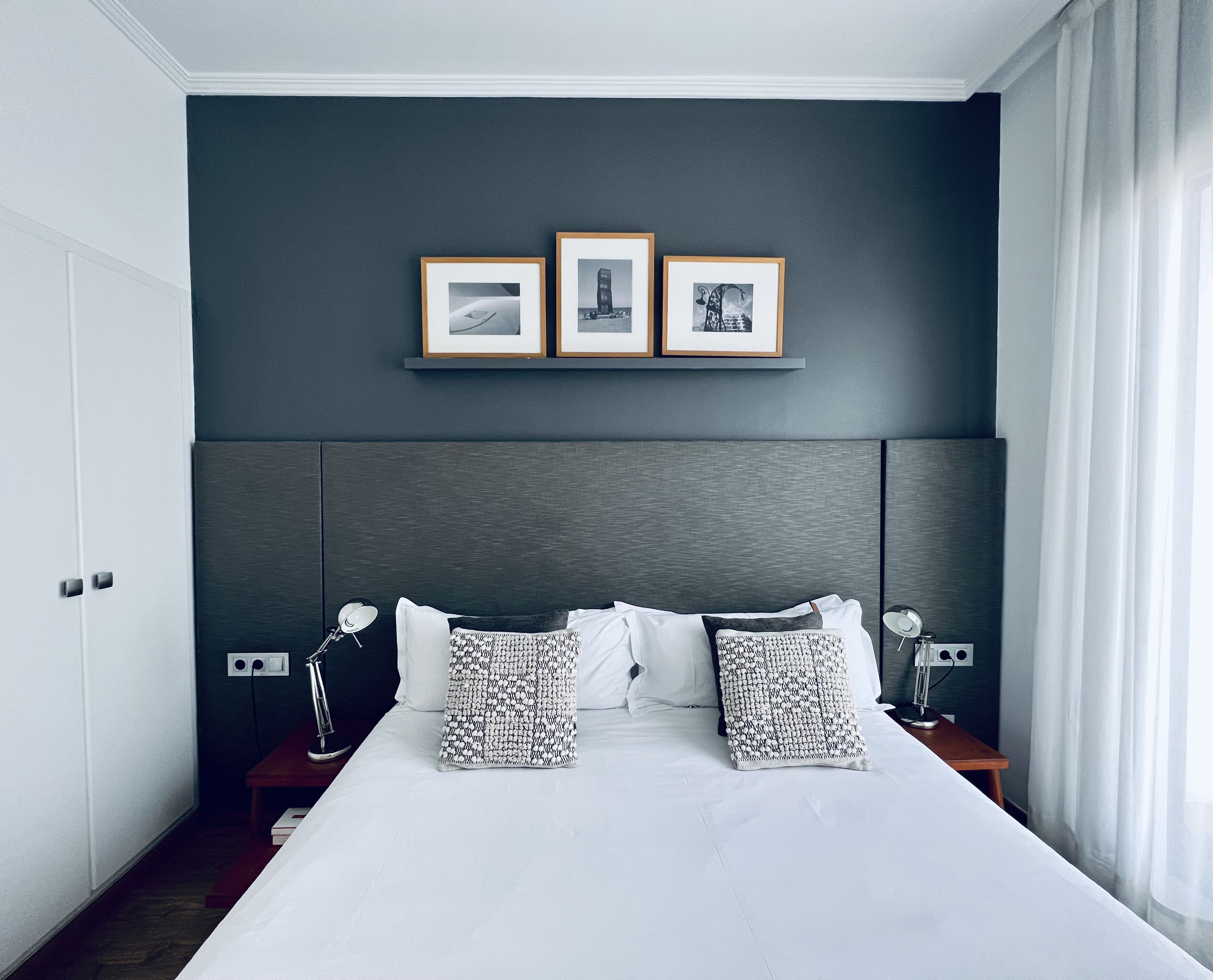 Una habitación de hotel moderna con una cama grande, paredes oscuras y tres cuadros en la pared.