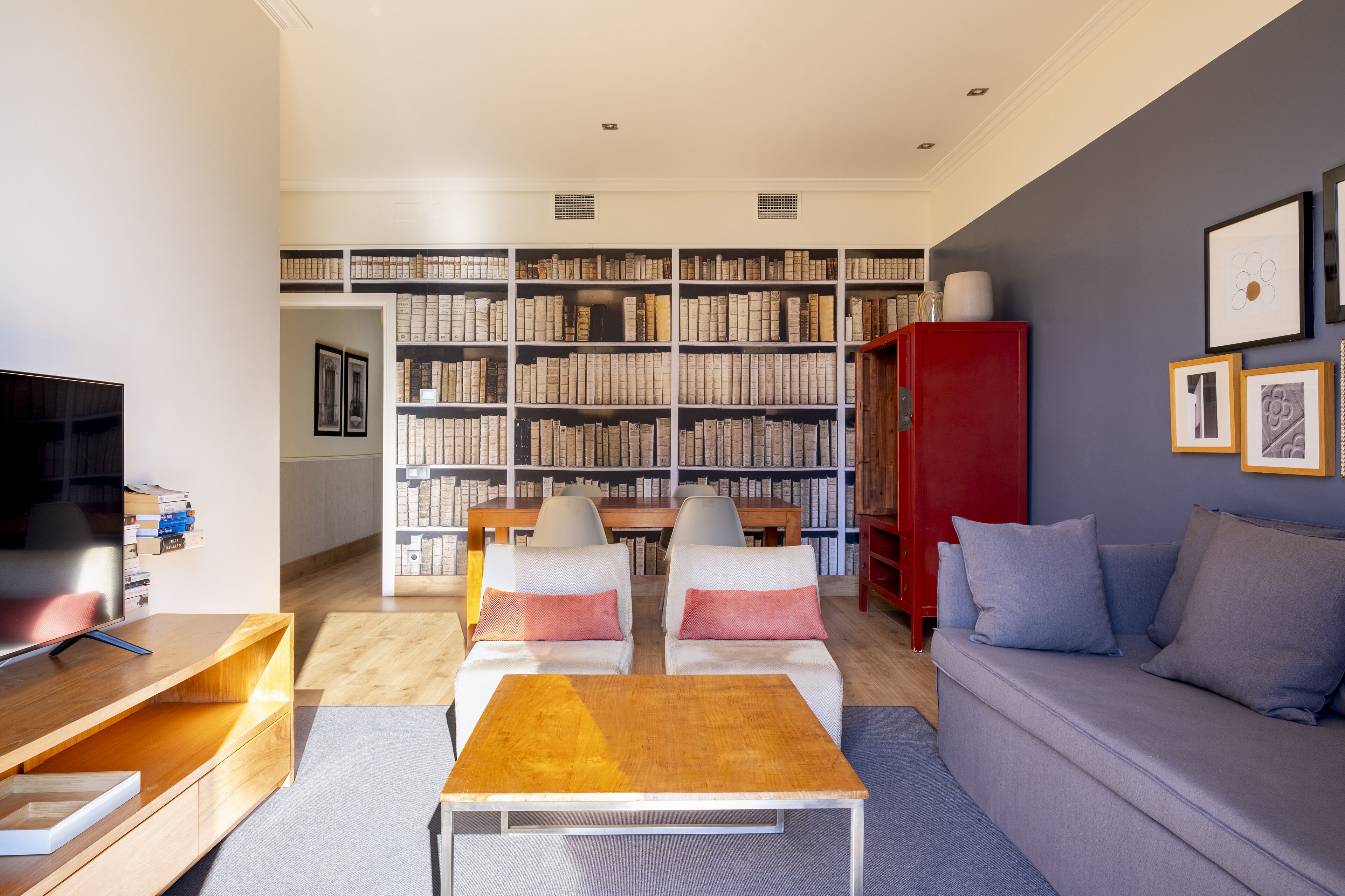 A modern living room with a large bookshelf, a red cabinet, a grey sofa, and a wooden coffee table.