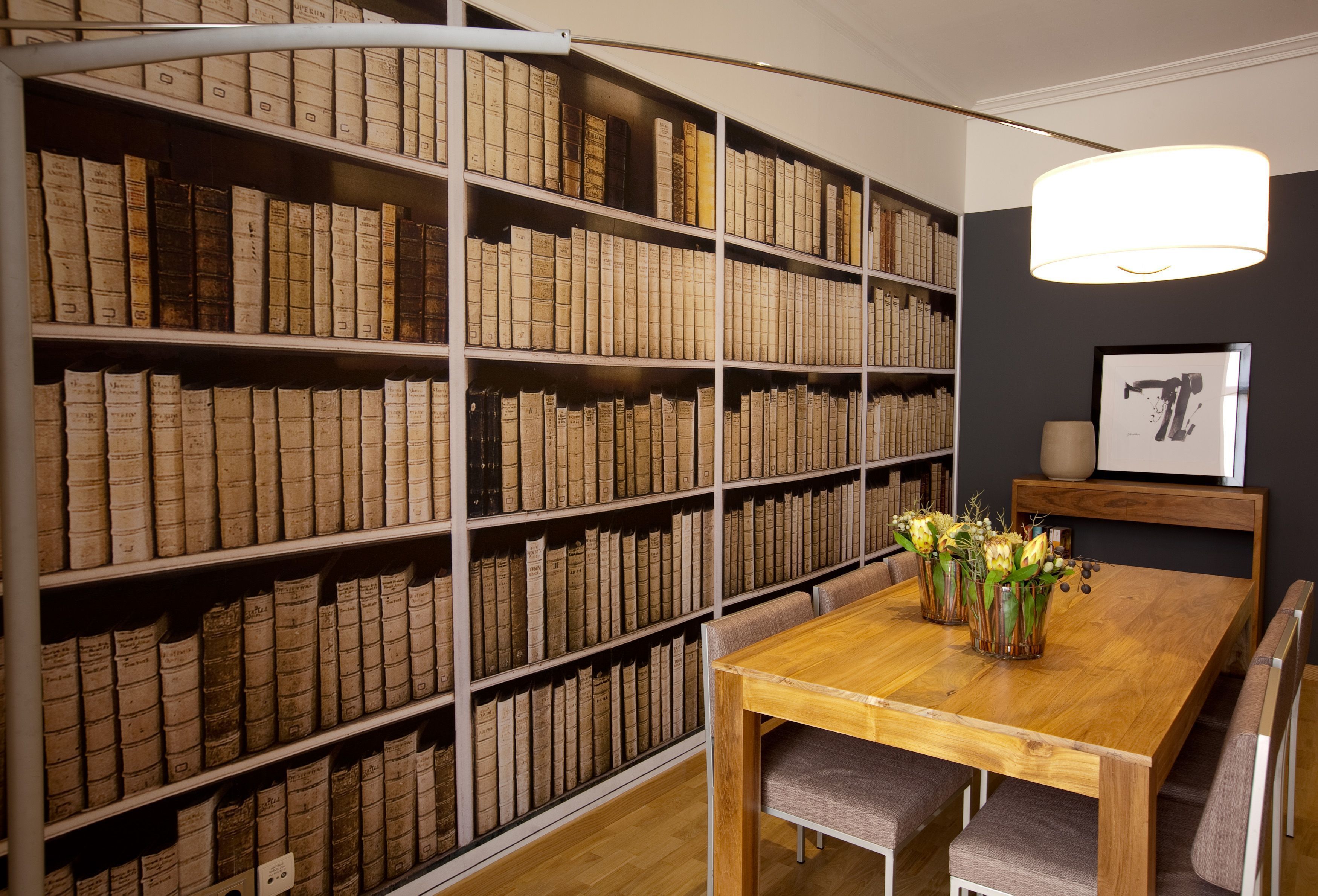 Una habitación con una mesa y sillas de madera, rodeada de altas estanterías llenas de libros.