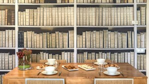 Una mesa de comedor dispuesta con platos, tazones y vasos, rodeada de estanterías llenas de libros.