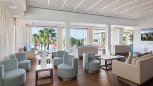 Un vestíbulo amplio con mobiliario moderno, ventanas grandes y vistas a palmeras.