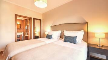A hotel room with two beds, a mirror, a nightstand with a lamp, and a bathroom visible through an open door.