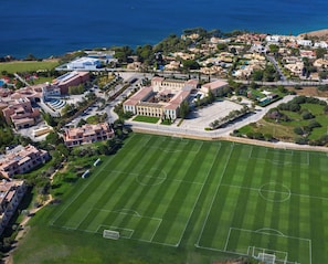 An aerial view of a residential area with a large green sports field, buildings, and a coastline.