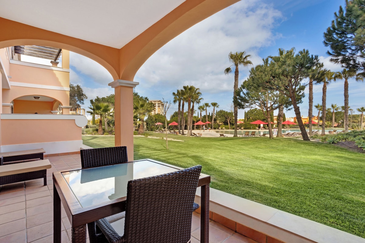 An outdoor patio with a glass-top table and wicker chairs, overlooking a well-maintained lawn and palm trees.