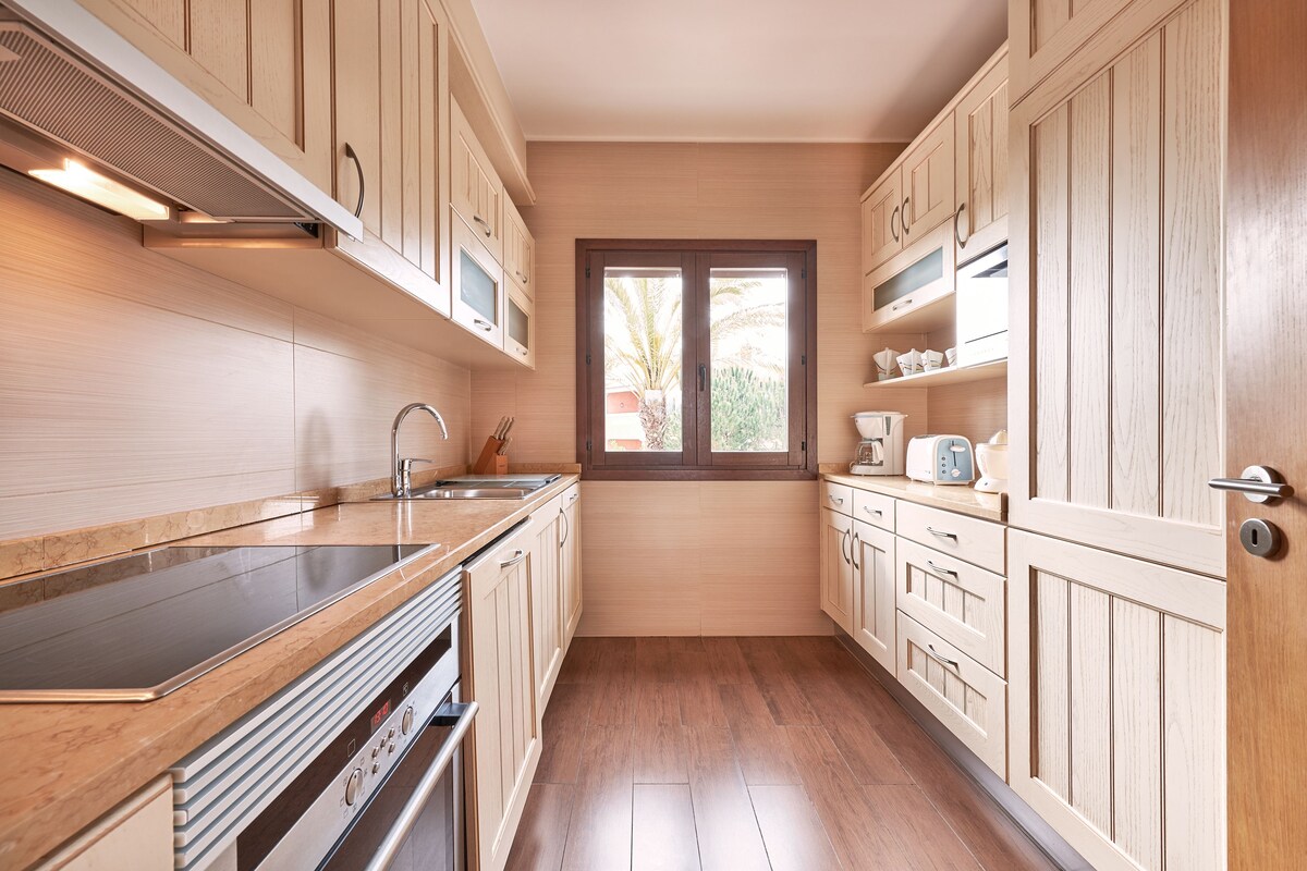 A kitchen with wooden cabinets, a stainless steel countertop, and a window with a view.