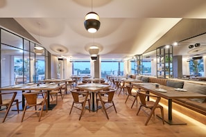 A modern dining area with tables, chairs, and a seating area with a view. - Cascade Wellness Resort Lagos Algarve by Domes (Lagos)