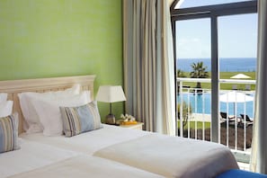 Habitación de hotel con cama, mesita de noche con lámpara y vista a una piscina y al océano.