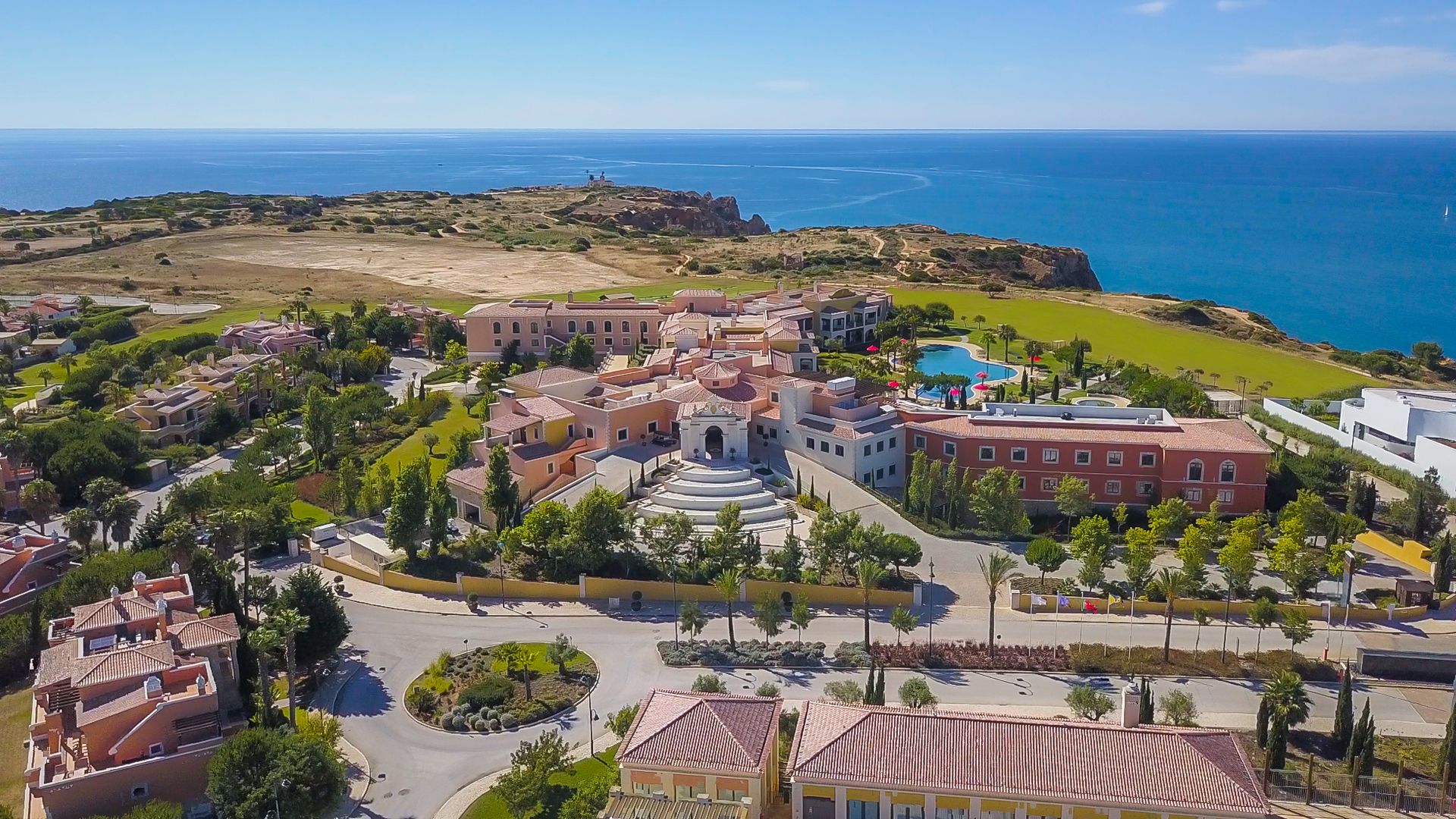 Eine Vogelperspektive eines Küstenresorts mit einem zentralen Innenhof, umgebenden Gebäuden und Blick auf das Meer.