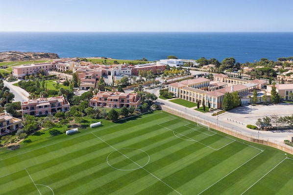 A residential area with a large green field, buildings with red roofs, and a view of the ocean.