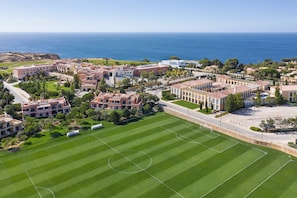 A residential area with a large green field, buildings with red roofs, and a view of the ocean.