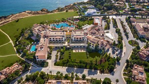 An aerial view of a coastal resort with multiple buildings, a central swimming pool, and a landscaped area. - Cascade Wellness Resort Lagos Algarve by Domes (Lagos)