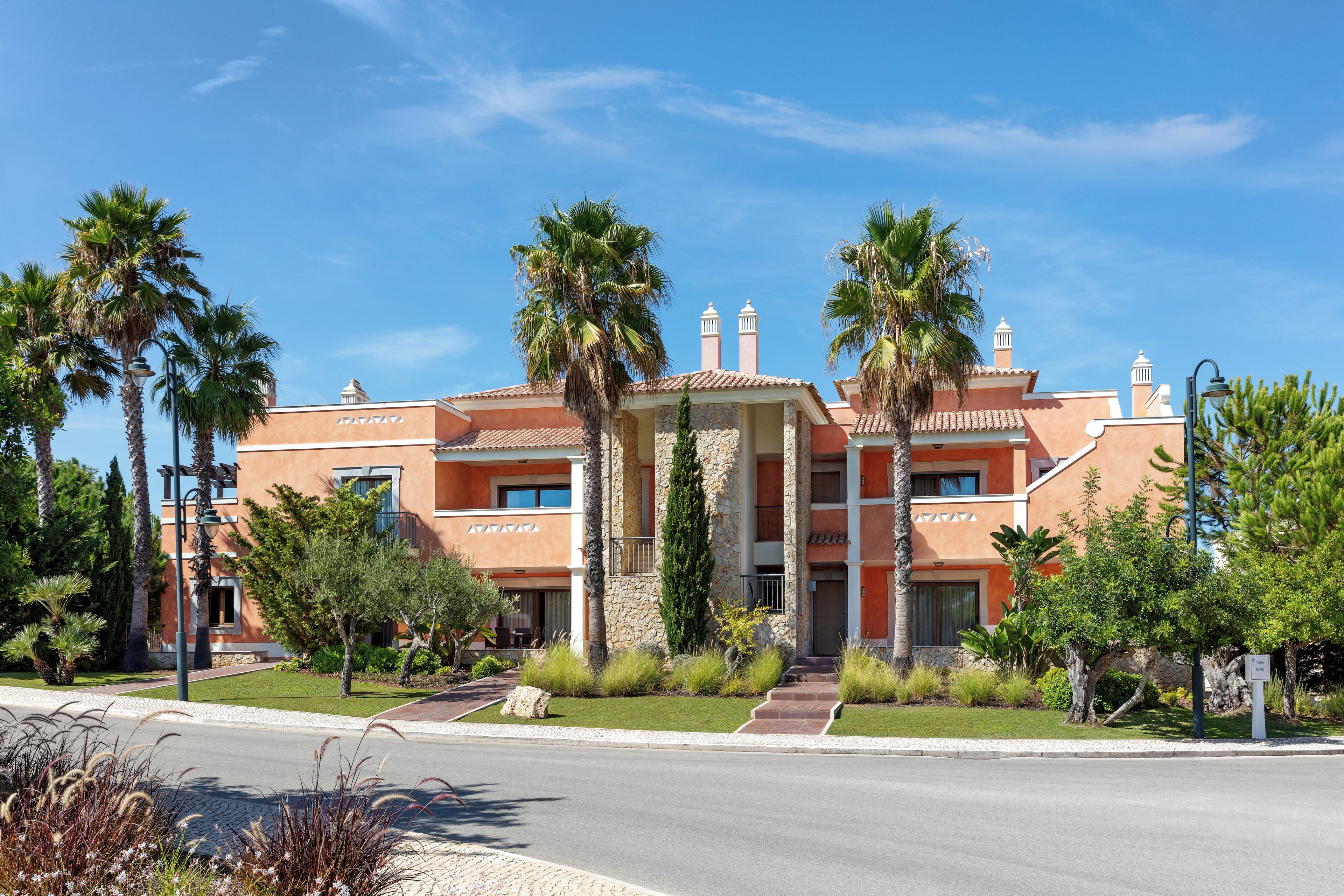 A hotel with a stone facade, multiple balconies, and palm trees.