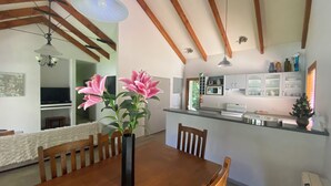 A dining area with a wooden table, chairs, a vase with flowers, and a kitchen in the background. - Resort Arrowtown (Speargrass Flat)