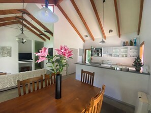 A dining area with a wooden table, chairs, a vase with flowers, and a kitchen in the background. - Resort Arrowtown (Speargrass Flat)