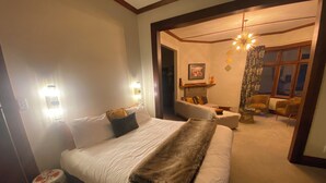 A bedroom with a large bed, two bedside lamps, a sofa, a chair, and a fireplace. - Resort Arrowtown (Speargrass Flat)