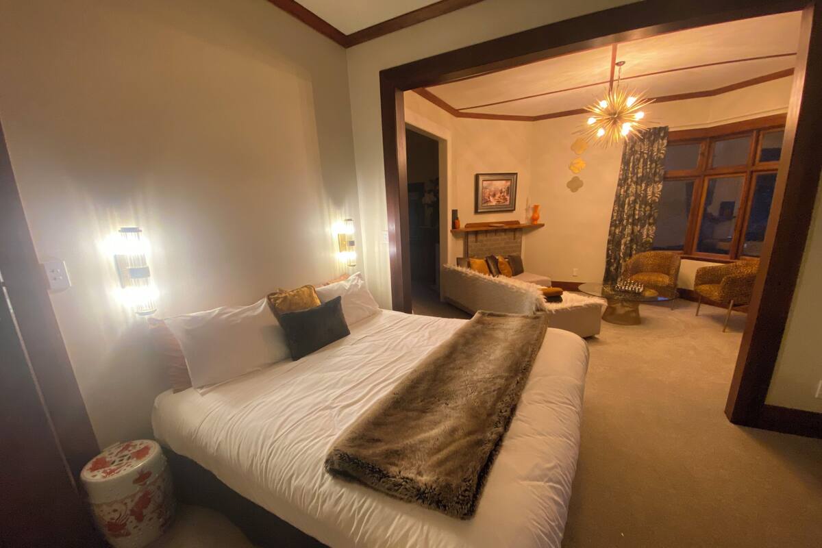 A bedroom with a large bed, two bedside lamps, a sofa, a chair, and a fireplace.