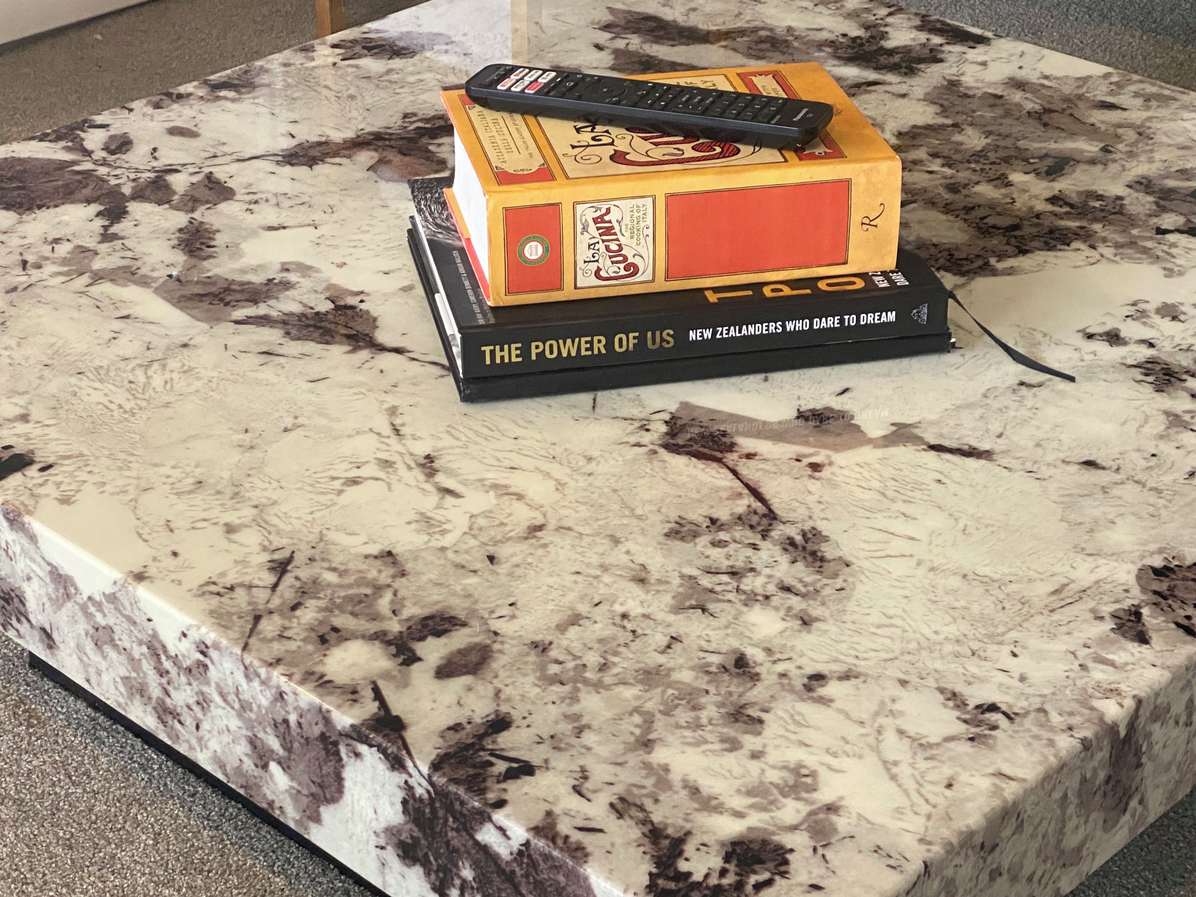 A book titled 'The Power of Us' on a marble table with a remote control on top.