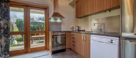 A modern kitchen with wooden cabinets, stainless steel appliances, and a view through the glass door.