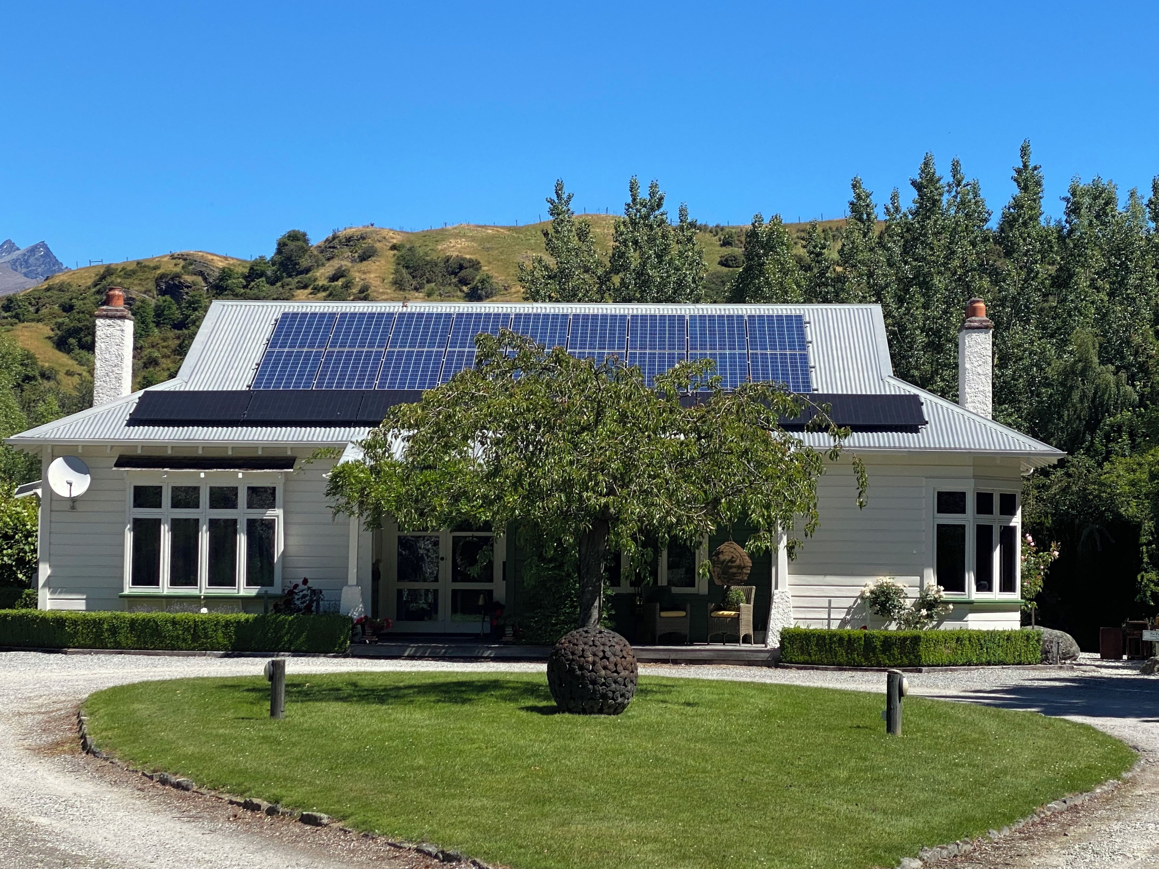 A house with solar panels, a well-maintained lawn, and a large tree in front.
