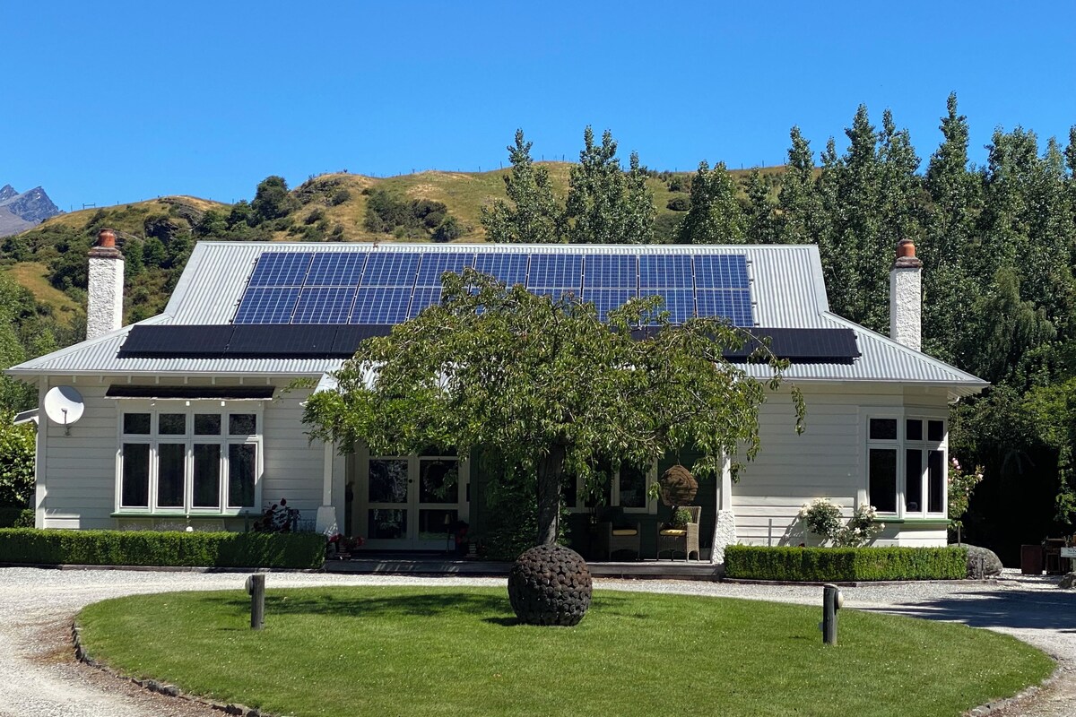 Una casa con paneles solares, un césped cuidado y un gran árbol en primer plano.
