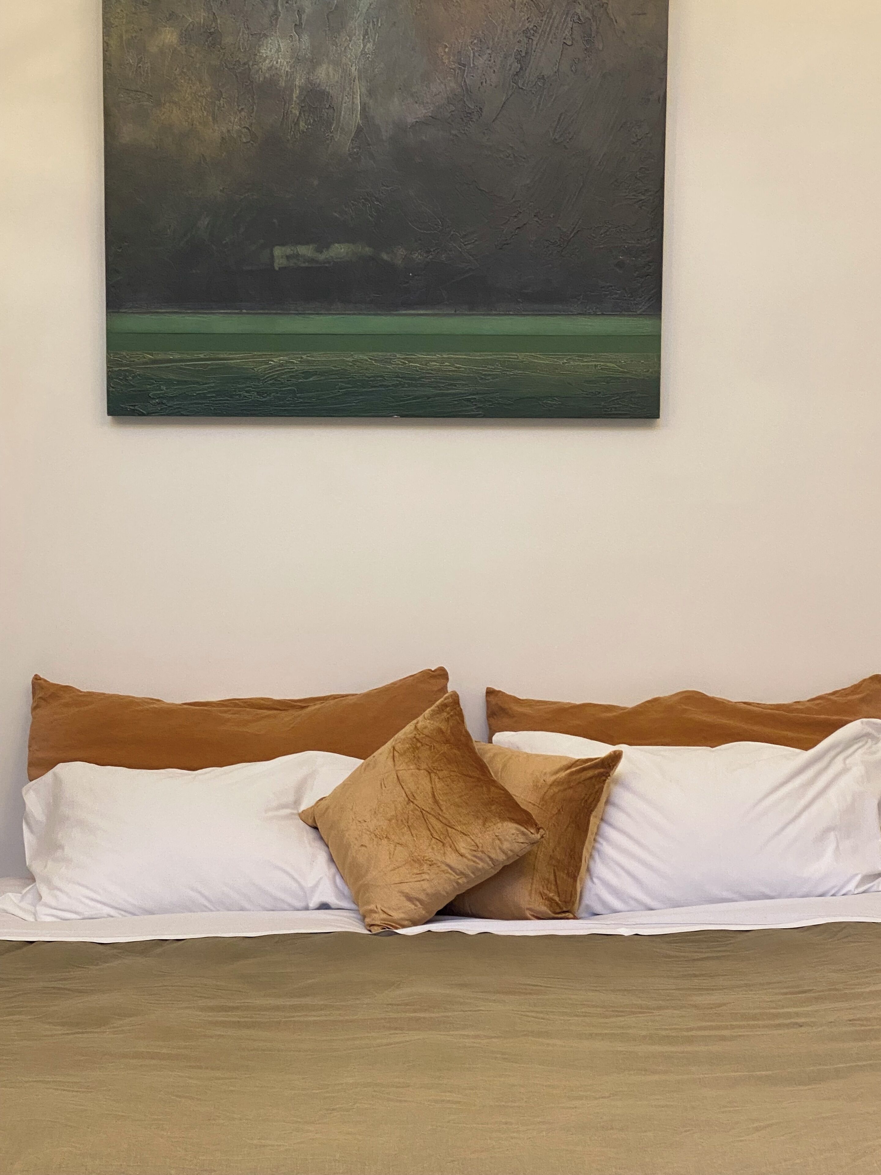 A bed with brown and white bedding, a painting of a stormy sea on the wall above, and a plain white wall.